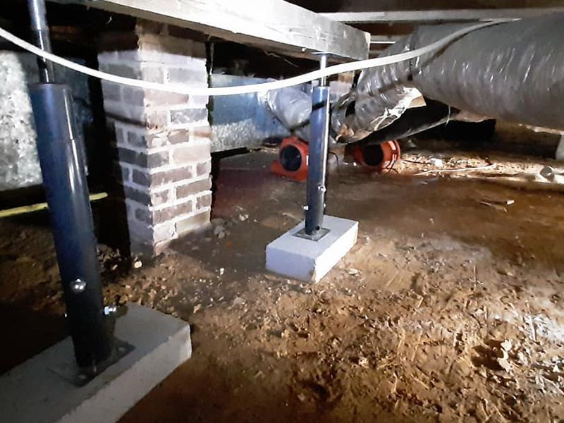Crawlspace with supports, brick, and ductwork. Dirt floor and two orange fans visible.