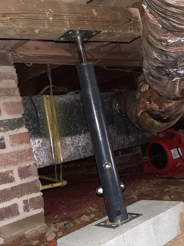 Black adjustable foundation support beam in a crawlspace, secured to a concrete base and a wooden beam.