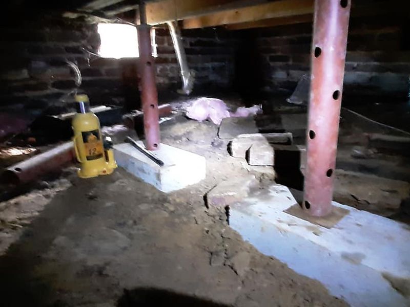 Crawlspace with jack and metal supports. Concrete blocks on dirt. Brick foundation.