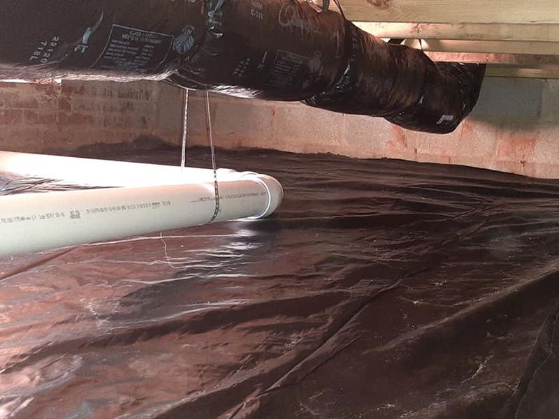 Black plastic vapor barrier in crawl space with pipe and ductwork.