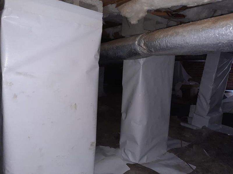 White-wrapped support columns in a crawl space, with ductwork overhead.