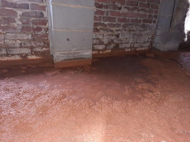 Damp, reddish-brown basement floor and brick walls; a concrete pillar stands in the center.