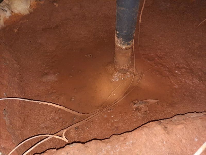 Muddy crawl space with a black pipe protruding from the soil.