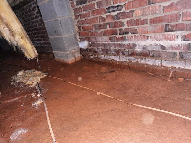 Crawl space with brick walls and a dirt floor.  Electrical wires lie across the dirt.