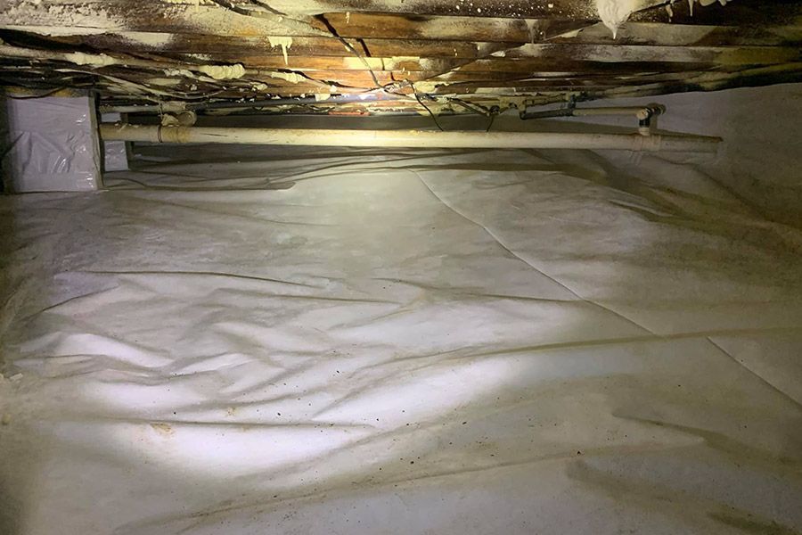 Crawlspace with white vapor barrier on floor, wooden beams above, signs of moisture, and some insulation.