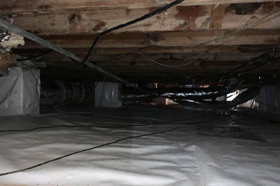 Underneath a home, a crawl space with vapor barrier and ductwork.