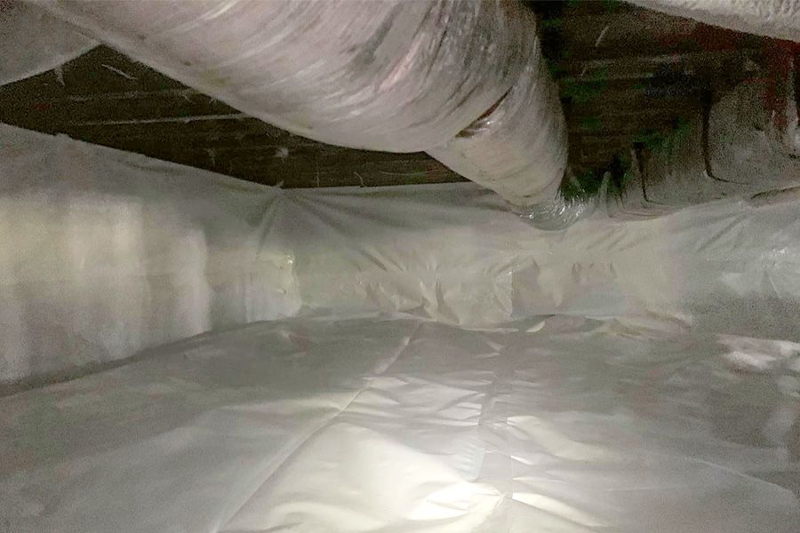 White plastic vapor barrier lining a crawl space under a house, with ductwork visible.