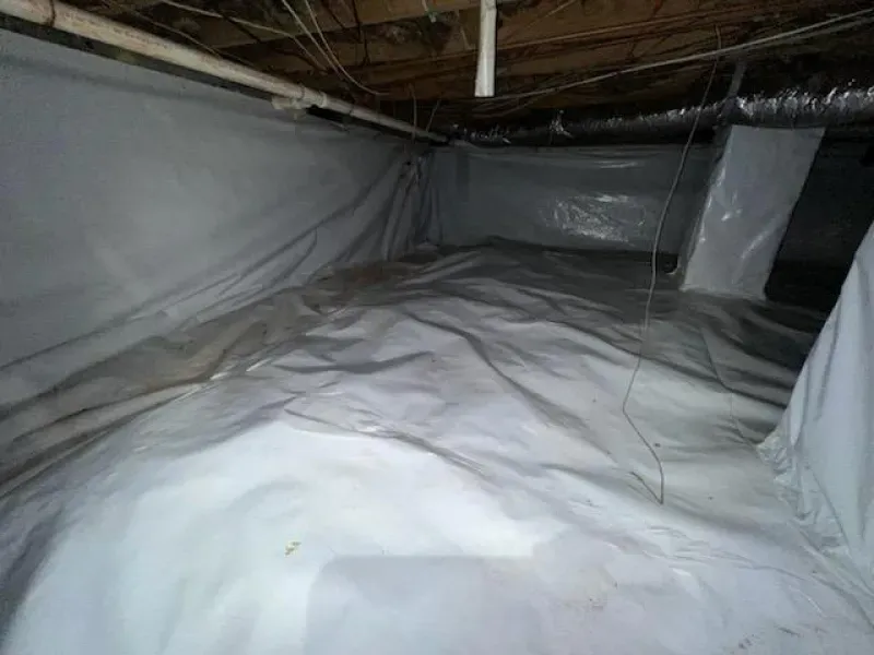 Crawl space with white plastic moisture barrier on walls and ground; pipes, ductwork visible.