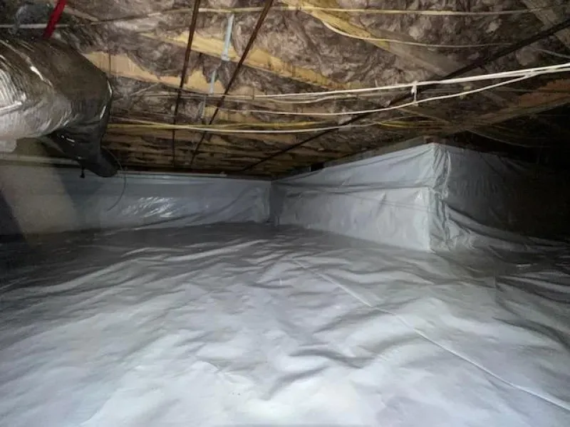 Crawl space with white vapor barrier on floor and walls, insulation above.