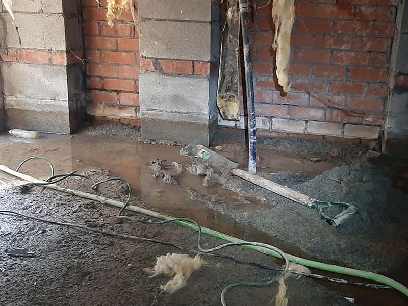 Construction site with water and tools on the floor near brick and concrete columns.