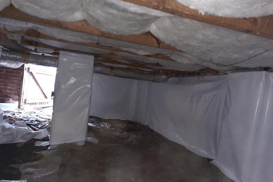 Crawl space with white plastic sheeting on walls and a dirt floor. Insulation visible on the ceiling.