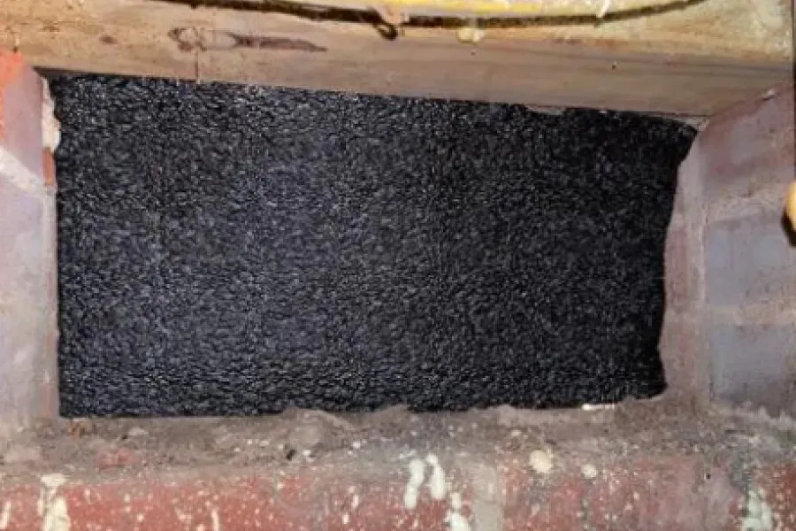 Rectangular opening filled with black insulation in a brick and wooden structure.