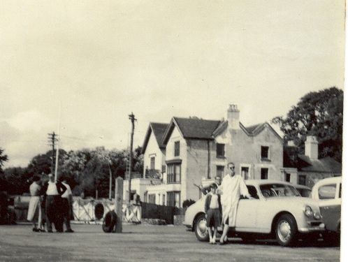 A black and white photo of a man standing next to a white car