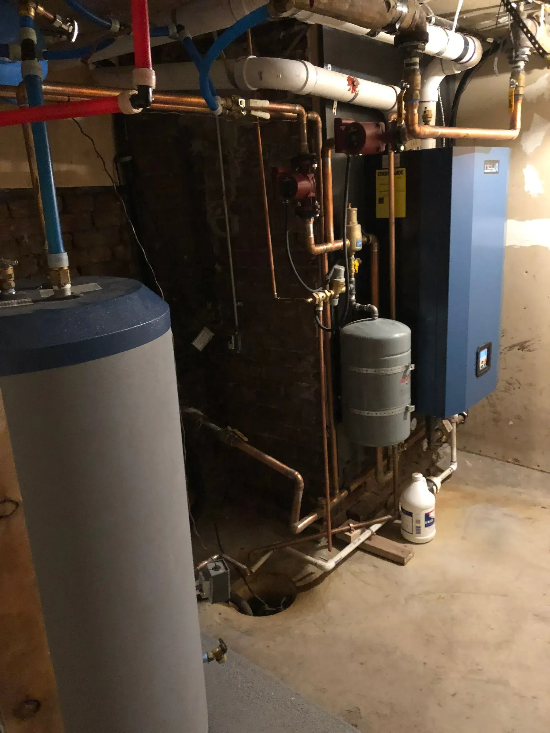A residential basement utility area with a blue water heater, a boiler, copper piping, and a gray expansion tank.