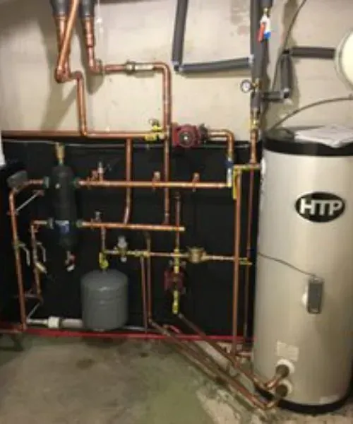 A copper-piped residential heating and hot water system featuring an HTP water tank and a small gray expansion tank.