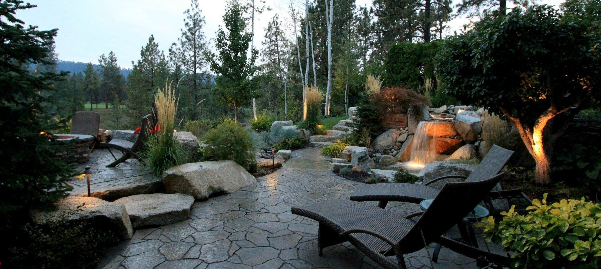 outdoor paver patio space with night lighting and water feature