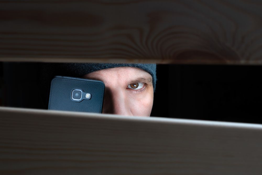 A Man Is Peeking Out From Under A Bed Looking At Her Cell Phone — Surveillance NQ In Cairns, QLD
