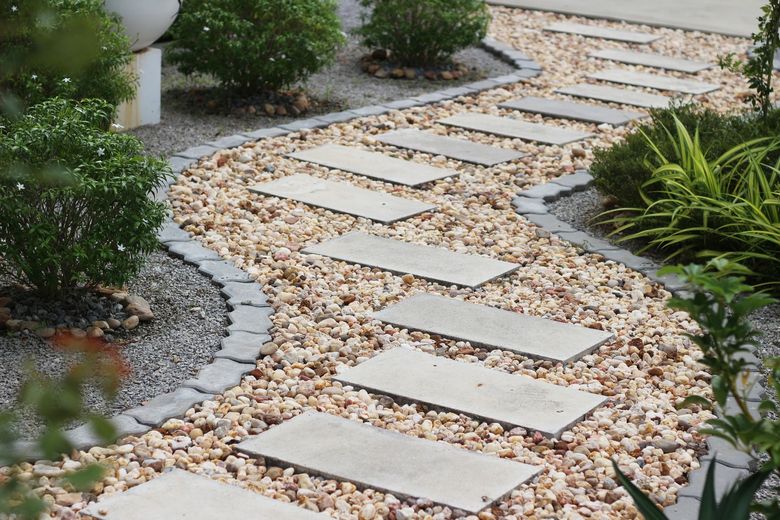 Stepping stones path through gravel and foliage in a garden.