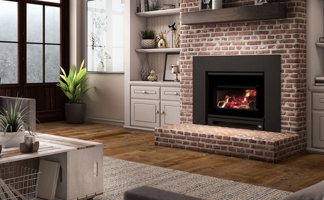 A cozy living room with a brick fireplace, a burning fire, built-in shelving, and indoor plants.