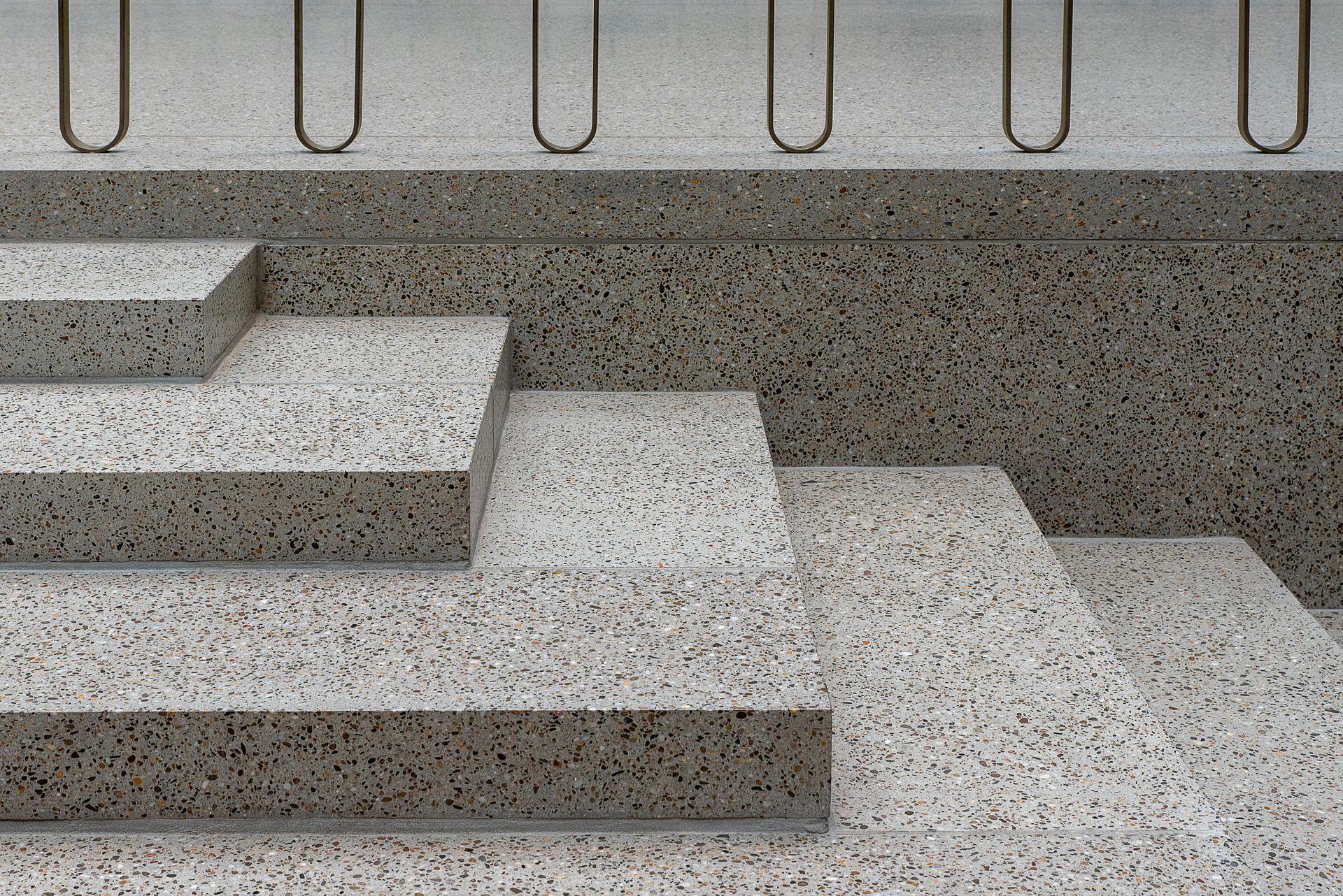 A set of three granite-textured steps leading up to a platform with a metal railing.