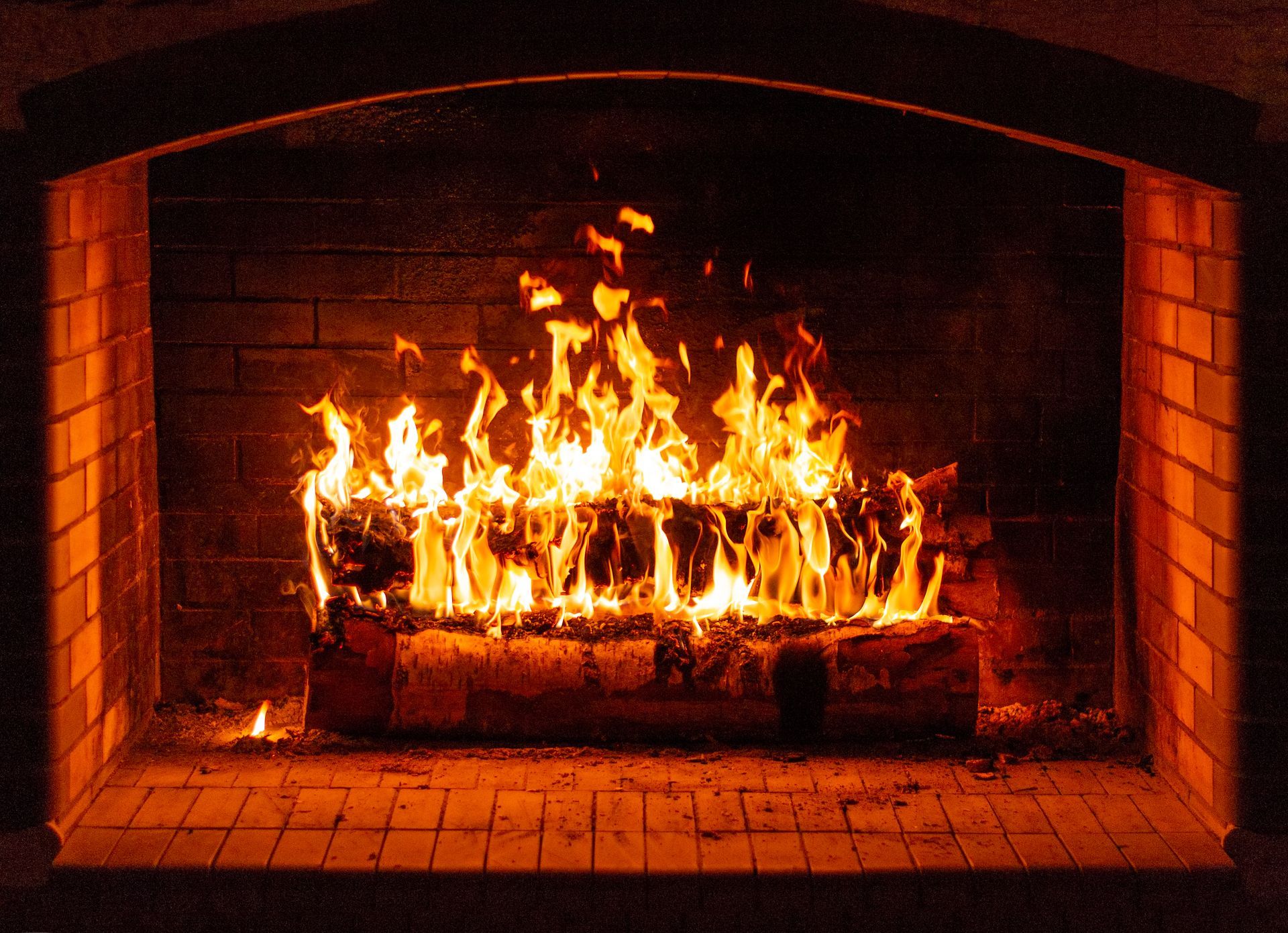 Fire burning in a brick fireplace, flames are orange and yellow, in a dark room.