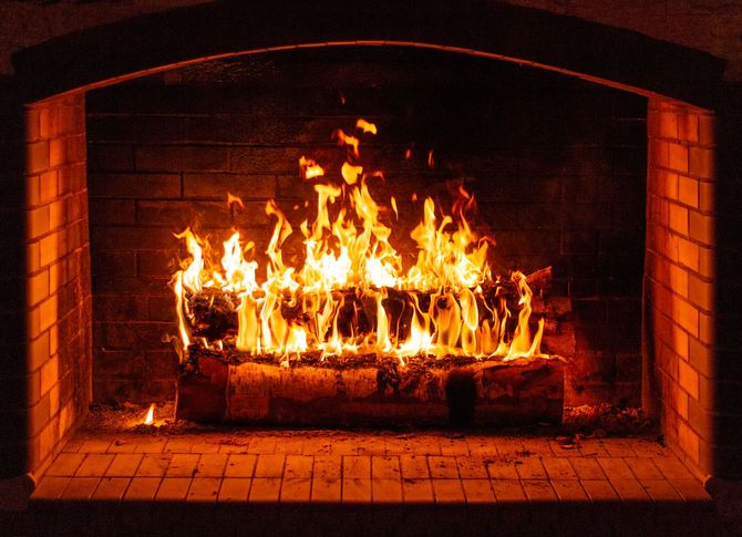 Fire burning in a brick fireplace, flames are orange and yellow, in a dark room.