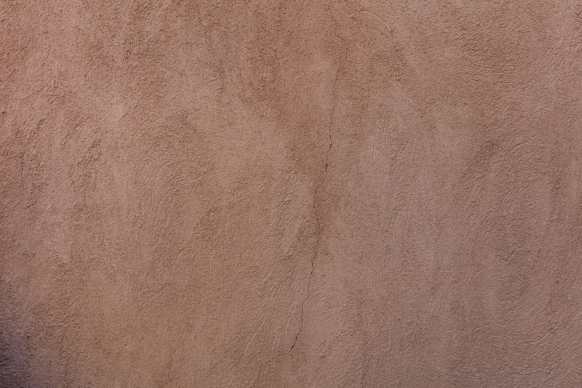 A close-up of a rough, brownish-tan wall texture with a fine-grained, stucco-like appearance.