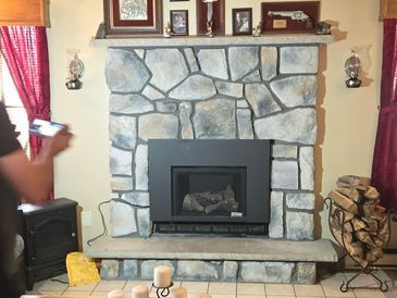 Fireplace with stone facade, black firebox, decorated with framed items and logs in a holder.