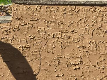 Textured, tan-colored stucco wall with a rough, uneven surface, possibly exterior.