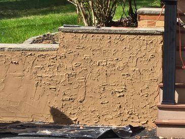 Tan stucco wall with textured finish, part of a landscape structure, with steps and green grass visible.