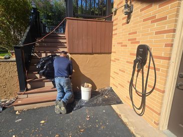 A person is applying stucco to a wall next to an electric vehicle charger, stairs, and a deck.