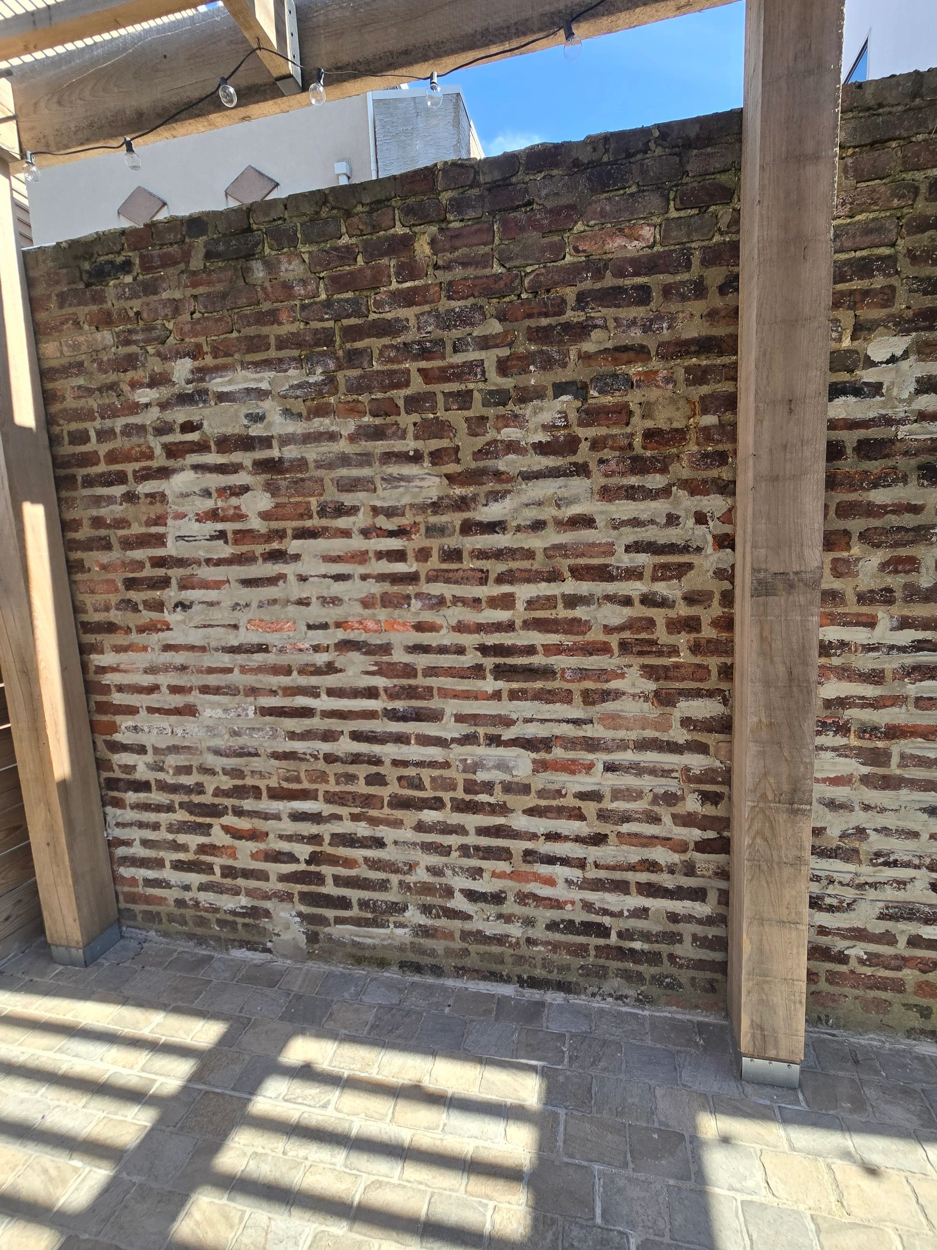 Brick wall with wooden beams in an outdoor setting, visible shadows and sunlight.