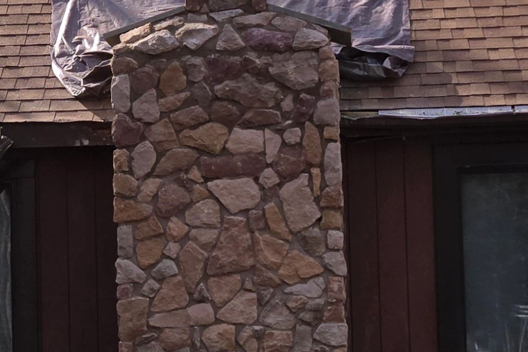 Stone chimney on a brown-shingled roof, partially covered by a tarp.