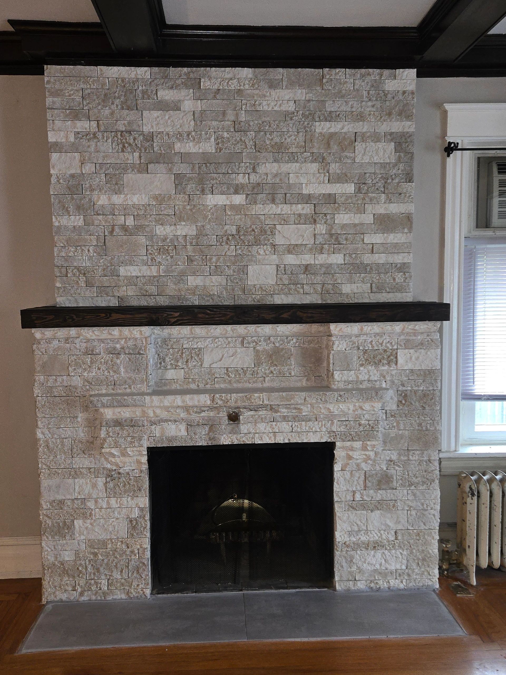 Fireplace with light stone facing, dark mantel, and black interior.