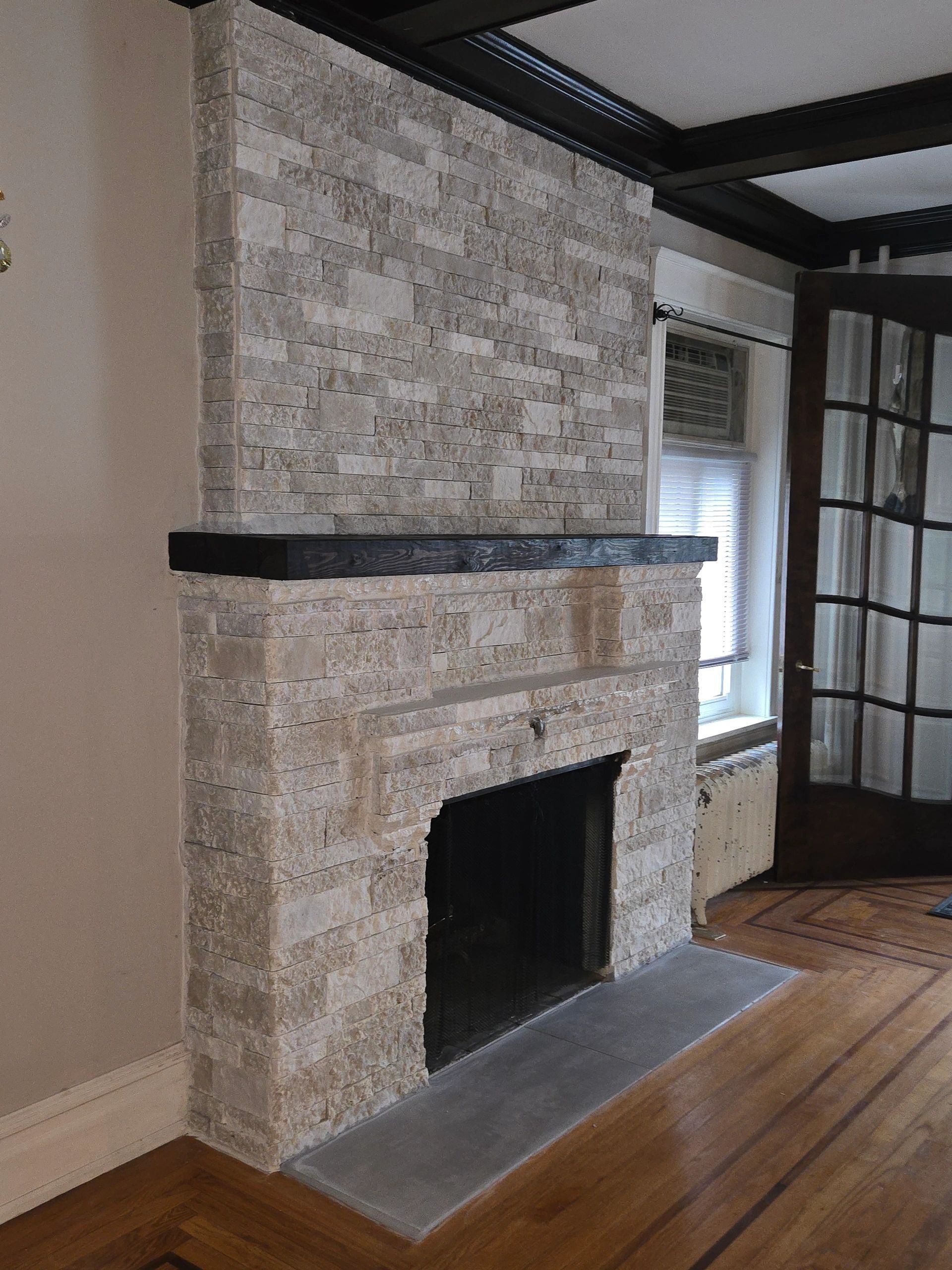 Fireplace with stone tile facade, dark mantel, and black interior. Wooden floor.