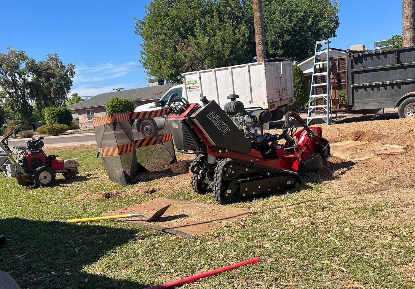 A tractor is cutting a tree stump in a yard.