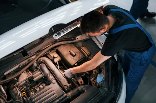 A man is working on the engine of a car in a garage.