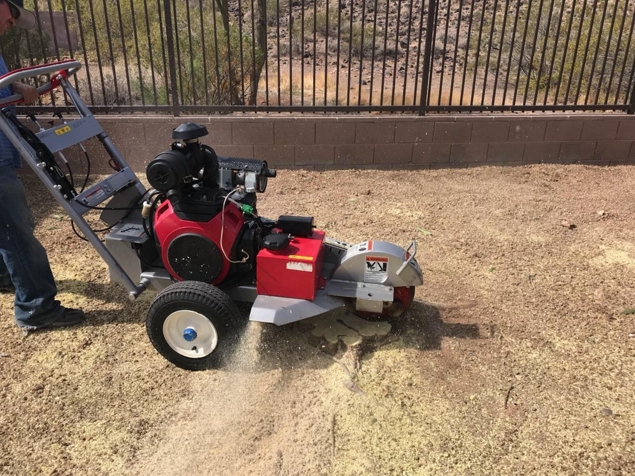 A man is using a stump grinder to remove a tree stump from a lawn.