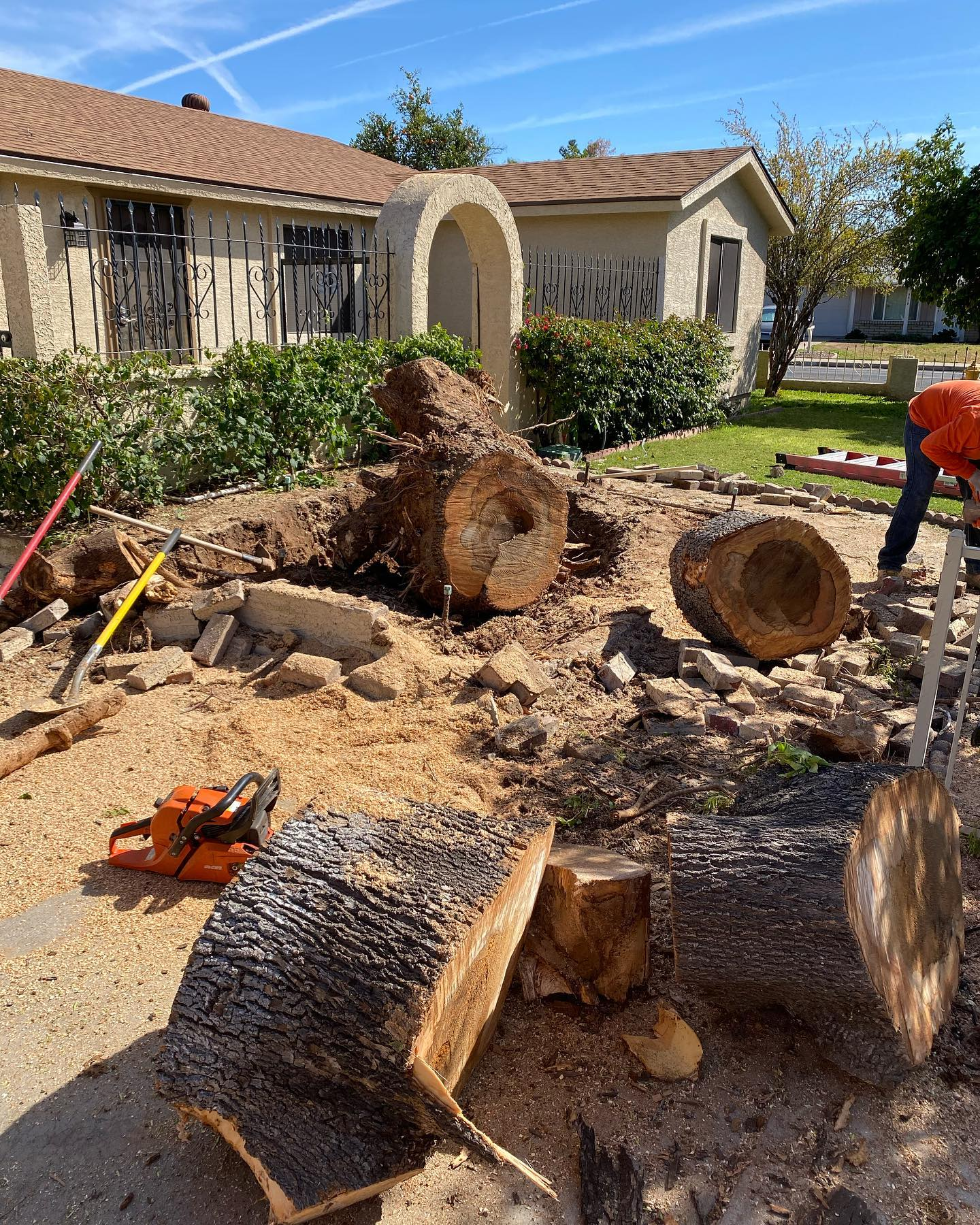 A man is cutting a tree stump with a chainsaw in front of a house.