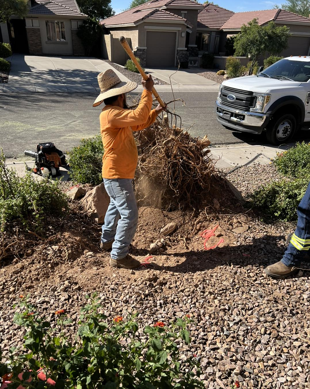 A man in a cowboy hat is raking a pile of rocks.