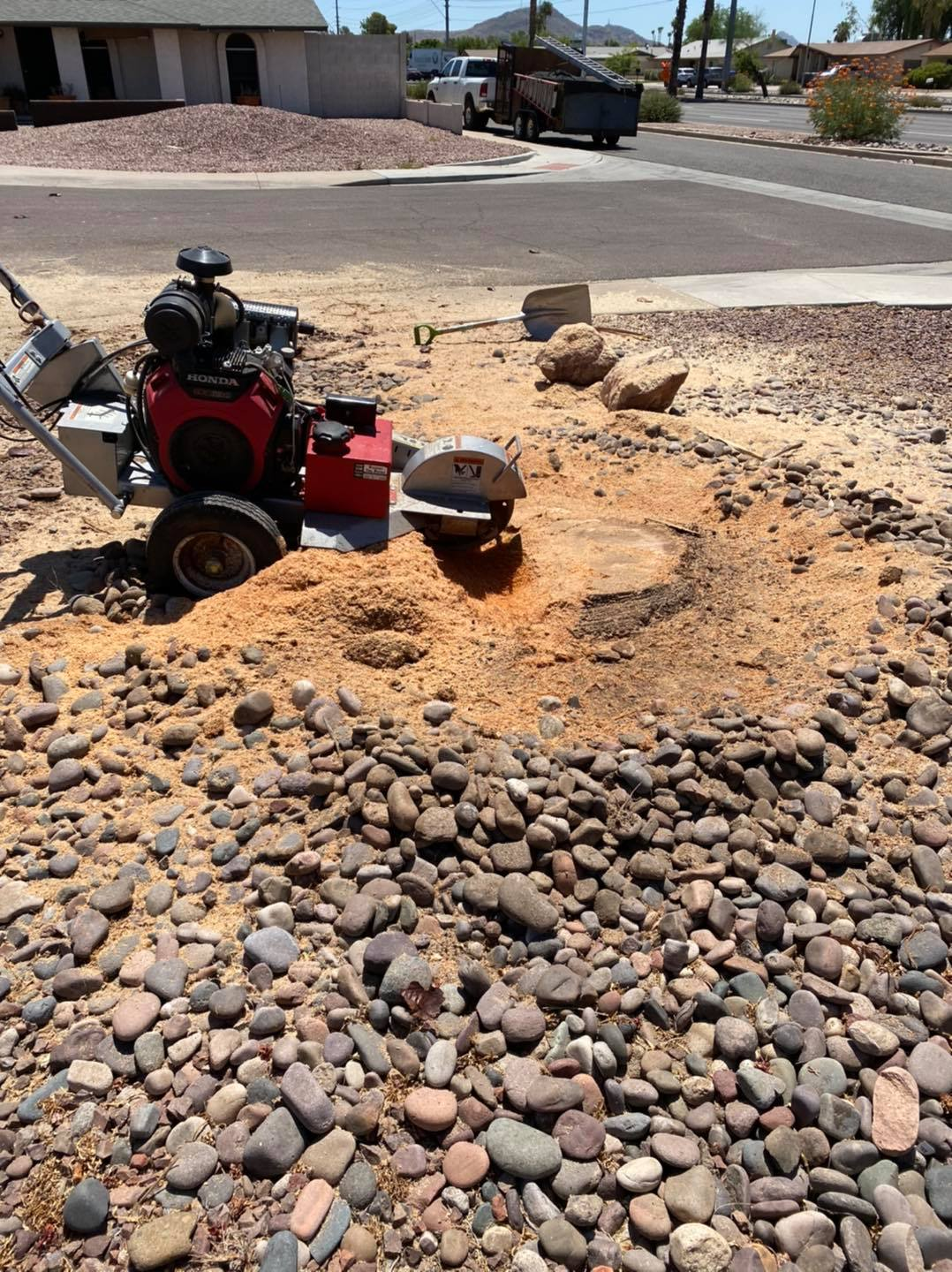 A tractor is cutting a tree stump in a pile of rocks.