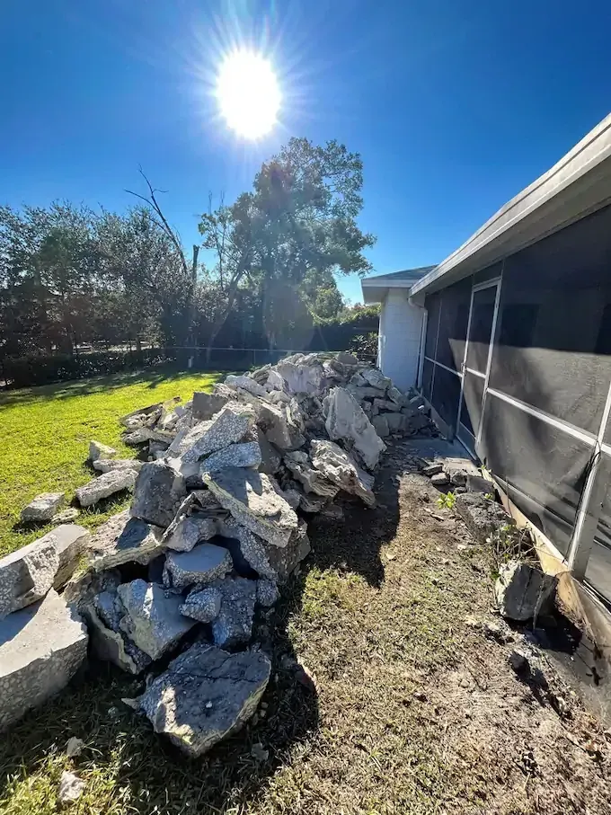 Pile of broken concrete debris next to a house under a sunny sky.