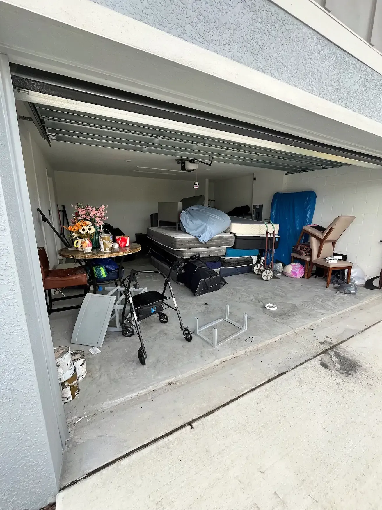 Cluttered garage interior. Mattresses, furniture, and miscellaneous items fill the space.