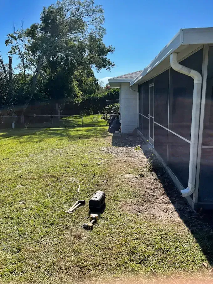 Green lawn next to a white house with a screened porch and tools.