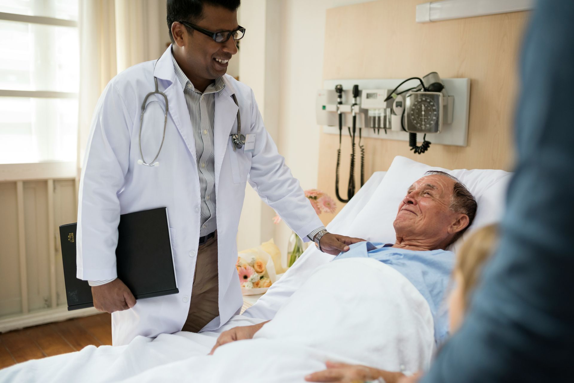 Doctor speaking with a patient in a hospital room while another person stands nearby.