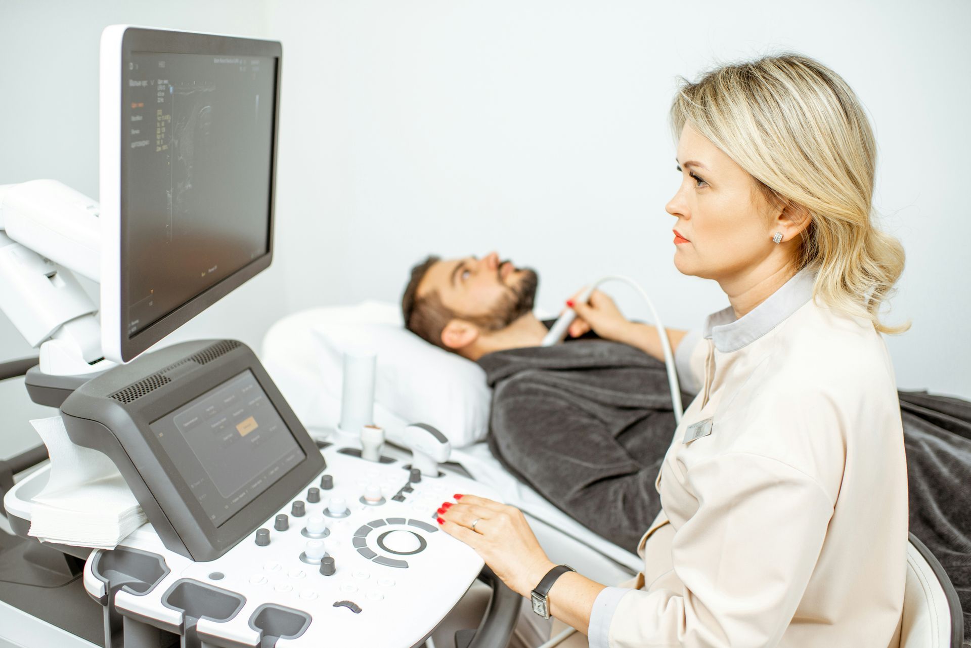 Ultrasound technician at a hospital monitor scanning a patient lying on an exam table
