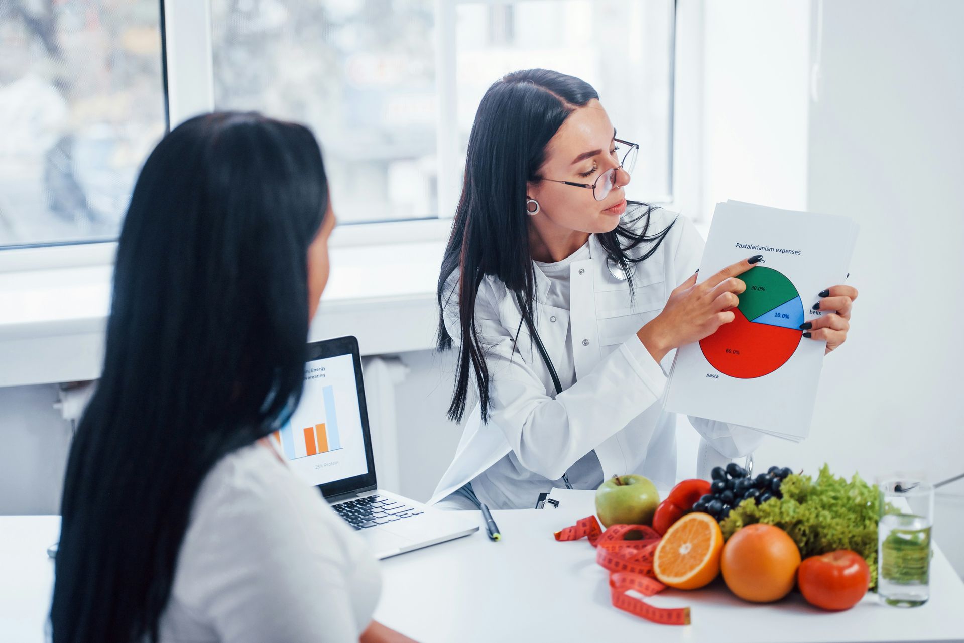 Nutritionist showing a colorful food chart to a client in a bright office, with fruit on the table