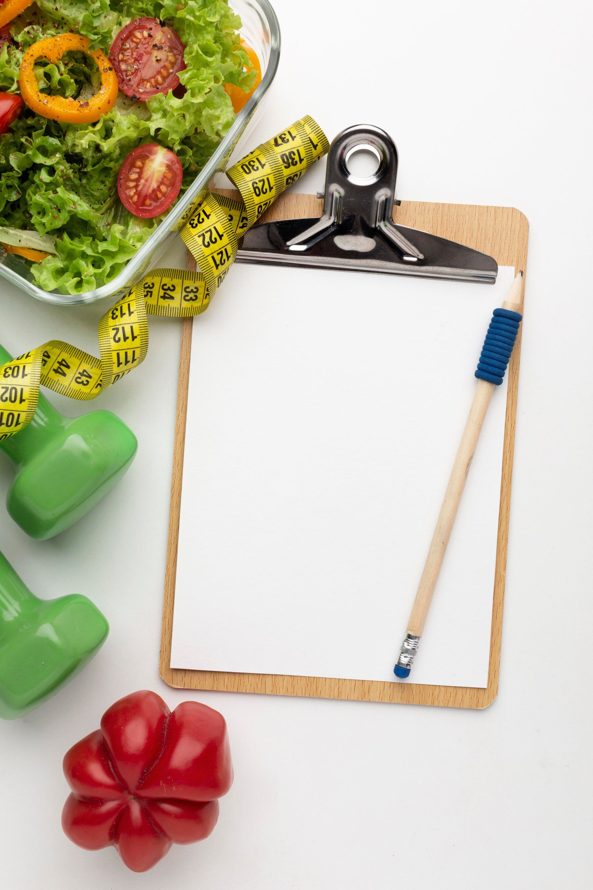 Clipboard with blank paper, measuring tape, dumbbells, salad bowl, and pencils on white background