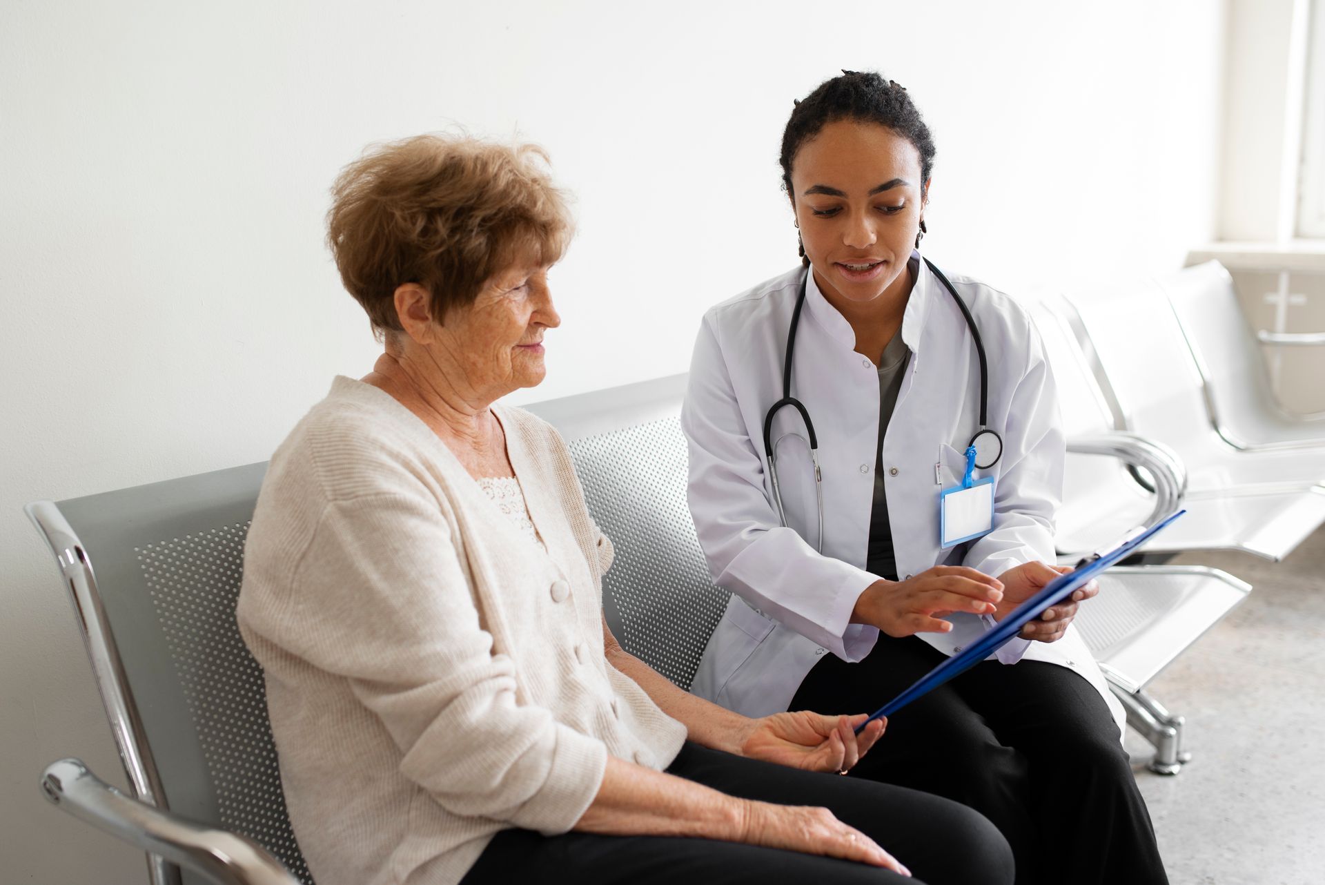 Doctor discussing a clipboard with a seated patient in a bright clinic waiting area
