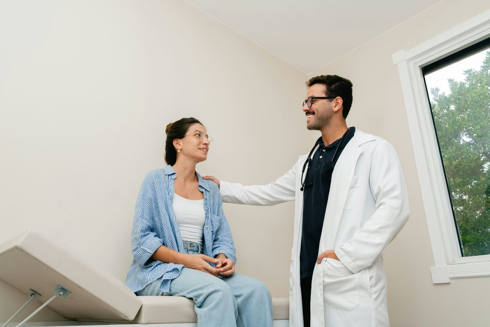 Doctor in white coat speaking with seated patient in a bright exam room